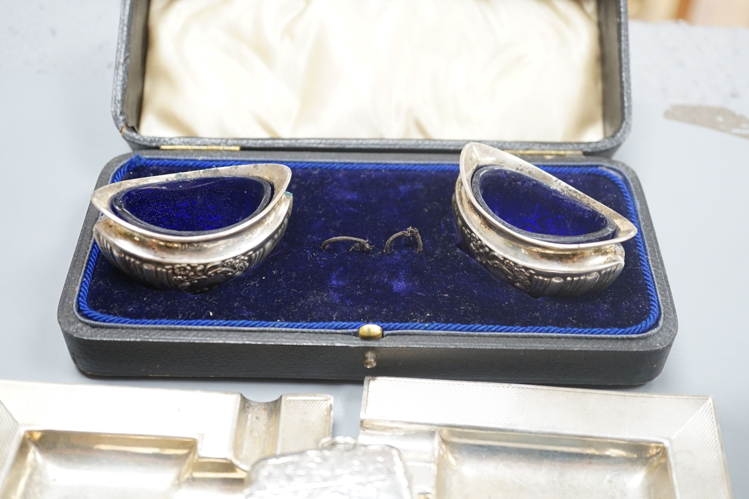 A pair of oval boat shaped salts, with blue glass liners and spoons, cased, Birmingham 1903, no spoons, a Victorian vesta case, all over flat chasing, Birmingham 1888, a pair of square ashtrays, with engine turned border